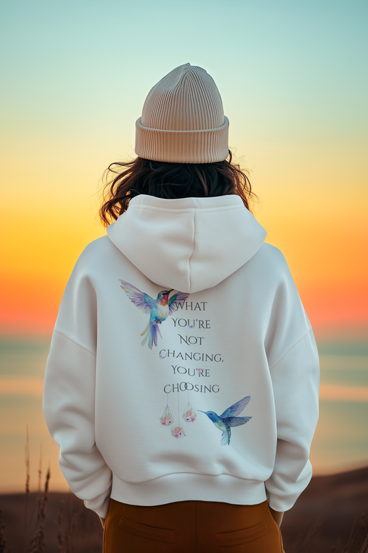 Person wearing a white hoodie with hummingbird designs and text, standing against a sunset landscape.