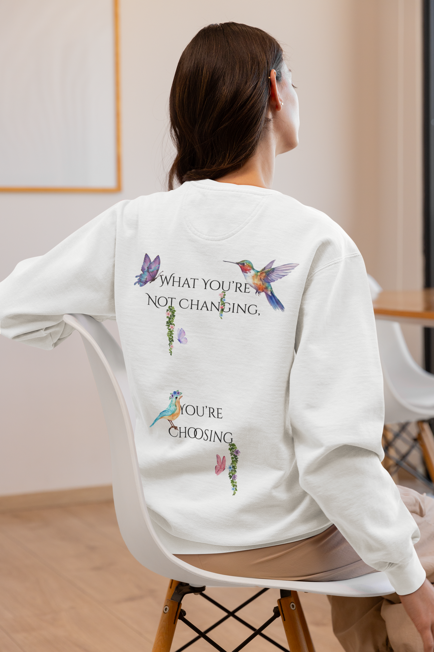 Person wearing a white sweatshirt with colorful designs and text on the back, sitting in a chair.