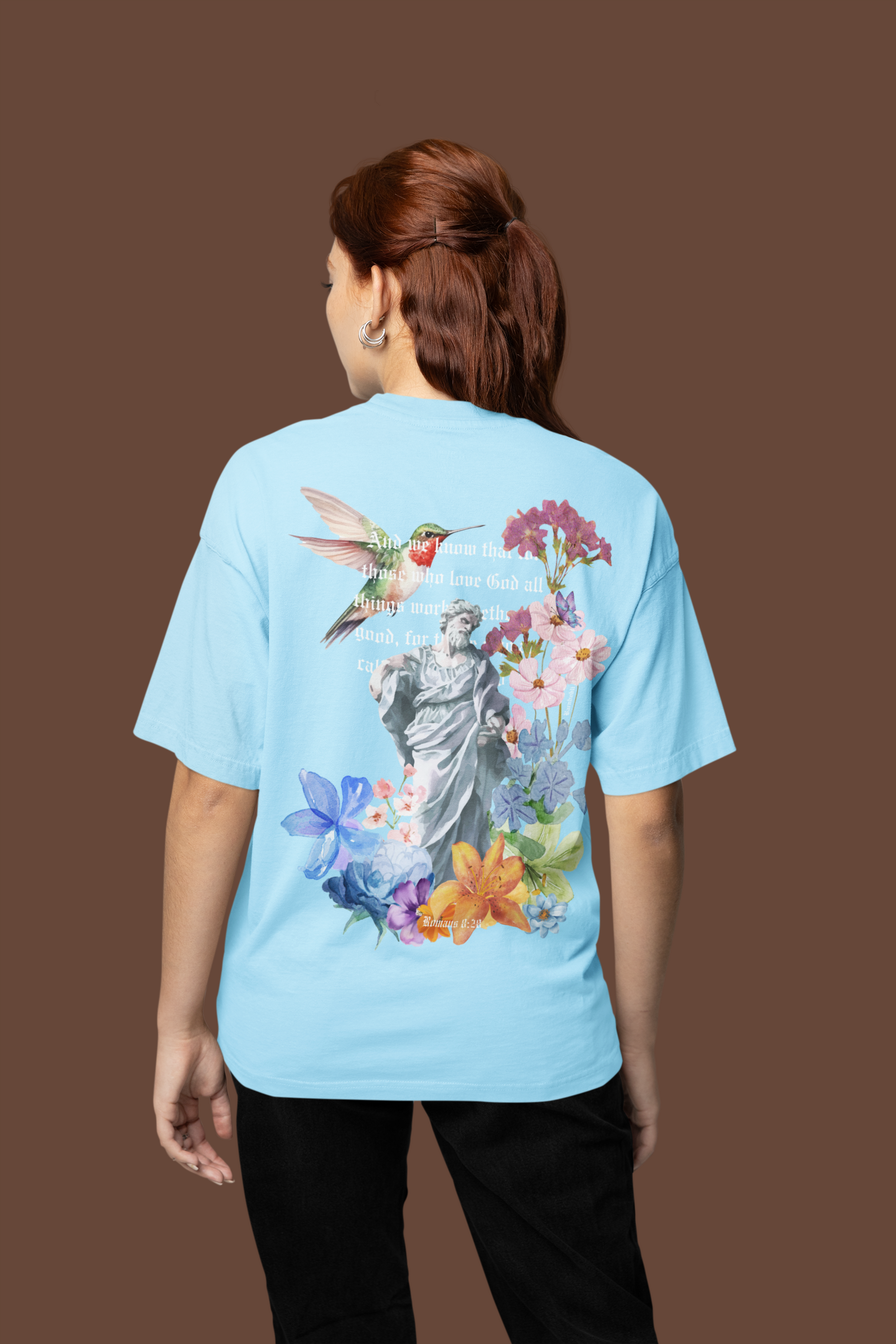 Person wearing a light blue t-shirt with a colorful design on the back against a brown background